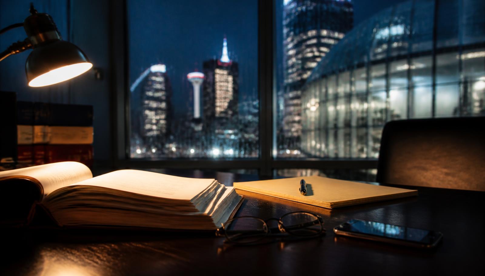 Calgary defence lawyer's desk at night with an open legal text and case file while preparing a bail plan, city skyline visible through the window